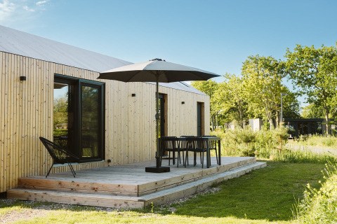 Modern tiny house at Holiday park De Klepperstee, Netherlands, featuring a deck, umbrella, and outdoor chairs.