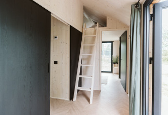 Interieur van tiny house Melle in De Klepperstee, met ladder naar de slaaploft en grote ramen.