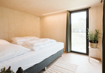 Chambre minimaliste d'une tiny house Melle au parc De Klepperstee, Pays-Bas, avec grand lit et lumière naturelle.
