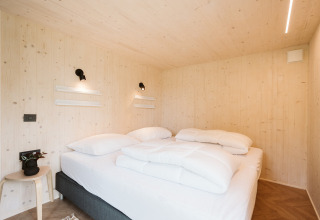 Soveværelse i tiny house 'Melle' på feriepark De Klepperstee, Nederlandene, med lyst træindretning.
