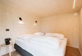 Slaapkamer van tiny house 'Melle' in vakantiepark De Klepperstee, Nederland, met lichte houtinrichting.