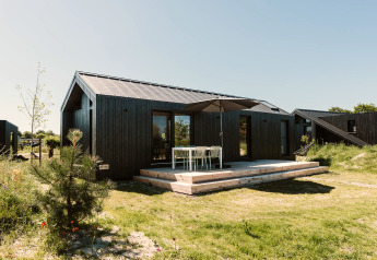 Sort træhytte med terrasse og havemøbler ved Holiday park De Klepperstee i Nederlandene på en solrig dag.