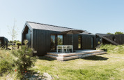 Zwart tiny house 'Est' met houten terras en tuinset bij De Klepperstee in Nederland op een zonnige dag.