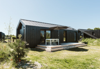 Zwart tiny house 'Est' met houten terras en tuinset bij De Klepperstee in Nederland op een zonnige dag.