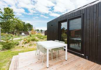 Terrasse extérieure avec table et chaises blanches près d’une tiny house noire à De Klepperstee, Pays-Bas.