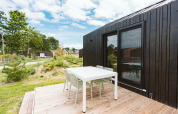 Buitenterras met witte tafel en stoelen naast een zwart tiny house bij De Klepperstee, Nederland.