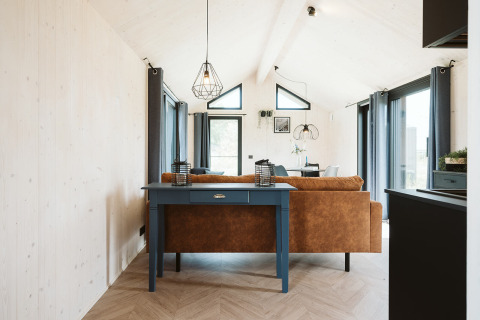 Interno della tiny house Est nel parco De Klepperstee, Paesi Bassi, con ampie vetrate e arredo moderno.