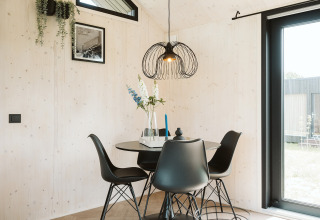 Sala da pranzo moderna nella tiny house Est al parco De Klepperstee, Paesi Bassi, con sedie nere e finestra.