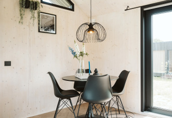 Sala da pranzo moderna nella tiny house Est al parco De Klepperstee, Paesi Bassi, con sedie nere e finestra.