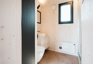 Baño minimalista en una tiny house del Holiday park De Klepperstee, Países Bajos, con paredes de madera clara.