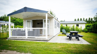 Casa pequeña Forest Lodge en Holiday Park Duinhoeve, Países Bajos, con porche y jardín con mesa.