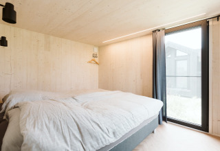 Camera da letto nella tiny house Est al parco vacanze De Klepperstee nei Paesi Bassi, con grande finestra.