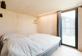 Slaapkamer in tiny house Est op vakantiepark De Klepperstee in Nederland, met groot raam.