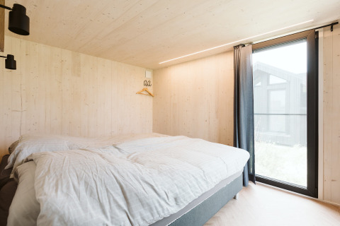 Slaapkamer in tiny house Est op vakantiepark De Klepperstee in Nederland, met groot raam.