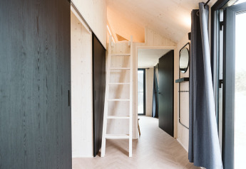 Interieur van een tiny house met loftladder, lichte houten muren en grote ramen bij De Klepperstee, Nederland.