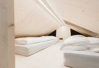 Dormitorio abuhardillado con dos camas y decoración minimalista en una tiny house en De Klepperstee, Holanda.