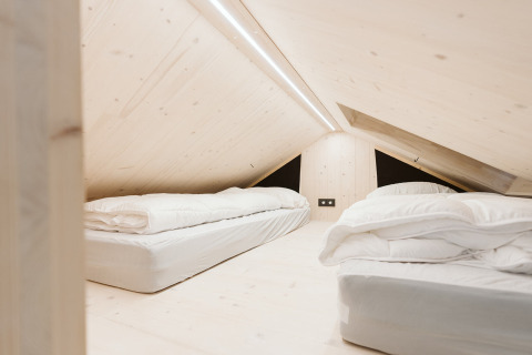 Dormitorio abuhardillado con dos camas y decoración minimalista en una tiny house en De Klepperstee, Holanda.