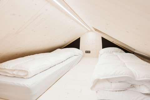 Camera mansardata con due letti singoli e legno chiaro nella tiny house Est al De Klepperstee, Paesi Bassi.