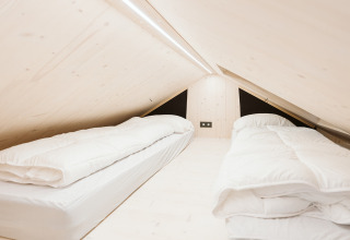 Camera mansardata con due letti singoli e legno chiaro nella tiny house Est al De Klepperstee, Paesi Bassi.