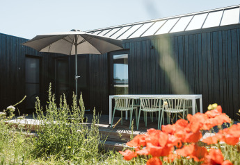 Buitenterras bij het tiny house Scandic op Holiday park De Klepperstee in Nederland, met bloemen en parasol.