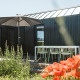 Buitenterras bij het tiny house Scandic op Holiday park De Klepperstee in Nederland, met bloemen en parasol.