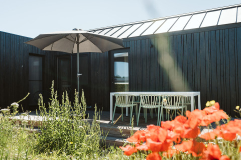 Buiten terras bij tiny house Scandic op Holiday park De Klepperstee in Nederland, met bloemen en parasol.