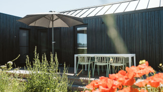 Buiten terras bij tiny house Scandic op Holiday park De Klepperstee in Nederland, met bloemen en parasol.