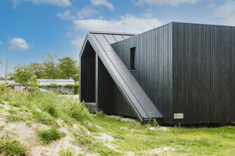 Pequeña casa moderna de madera negra Scandic en Holiday park De Klepperstee, rodeada de vegetación en los Países Bajos.