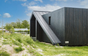 Pequeña casa moderna de madera negra Scandic en Holiday park De Klepperstee, rodeada de vegetación en los Países Bajos.