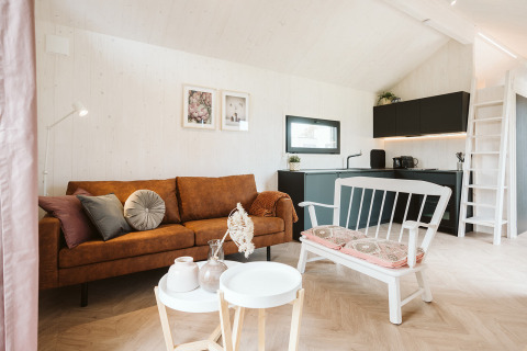 Interior moderno y acogedor de tiny house con sofá marrón, banco blanco y cocina elegante en De Klepperstee, Países Bajos.