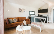 Interior moderno y acogedor de tiny house con sofá marrón, banco blanco y cocina elegante en De Klepperstee, Países Bajos.