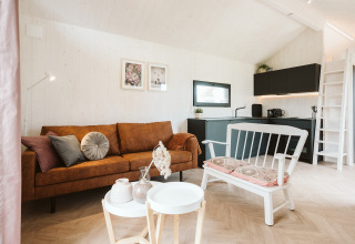 Modern, licht tiny house interieur met bruine bank, witte bank en open keuken bij De Klepperstee, Nederland.