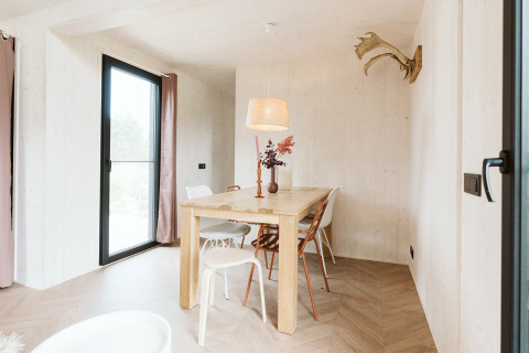 Luminoso comedor escandinavo en una tiny house del Holiday park De Klepperstee, con mesa y sillas de madera.