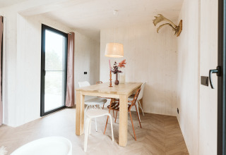 Luminoso comedor escandinavo en una tiny house del Holiday park De Klepperstee, con mesa y sillas de madera.