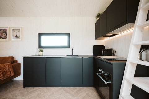 Moderne køkkenindretning i et tiny house ved Holiday park De Klepperstee med sorte skabe og træpaneler.