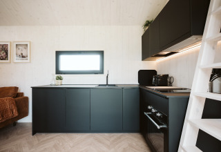 Cucina moderna in una tiny house presso Holiday park De Klepperstee, Paesi Bassi, con mobili neri e finestra.