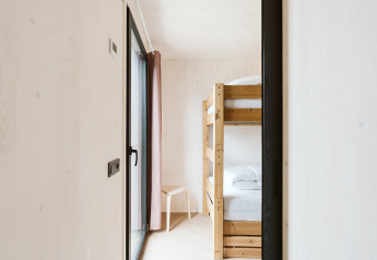 Dormitorio moderno y luminoso con litera y silla de madera en la tiny house Scandic en De Klepperstee, Países Bajos.