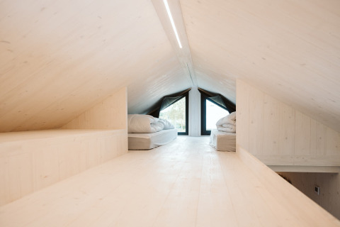 Buhardilla luminosa con camas y madera clara en la tiny house Scandic, Holiday park De Klepperstee, Países Bajos.