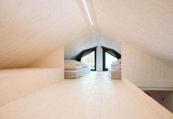 Buhardilla luminosa con camas y madera clara en la tiny house Scandic, Holiday park De Klepperstee, Países Bajos.