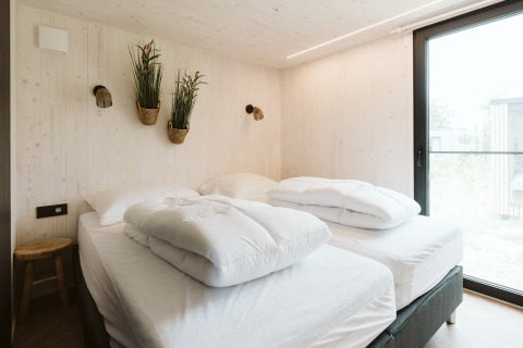Luminoso dormitorio en la tiny house Scandic en Holiday park De Klepperstee con dos camas y plantas.