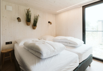 Lyst soveværelse i tiny house Scandic ved De Klepperstee, med to senge, planter og stort vindue.