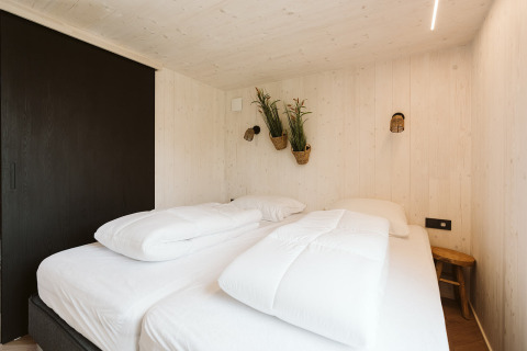 Slaapkamer van tiny house Scandic met twee bedden en hangende planten, Holiday park De Klepperstee, Nederland.