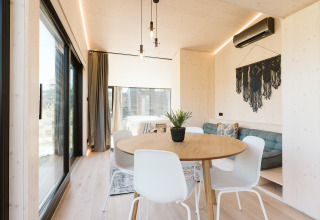 Interior luminoso y moderno de la tiny house Backer en Holiday park De Klepperstee, con comedor y sofá.