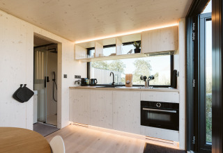 Modern tiny house kitchen at Backer, De Klepperstee, featuring open shelving, oven, and large windows.