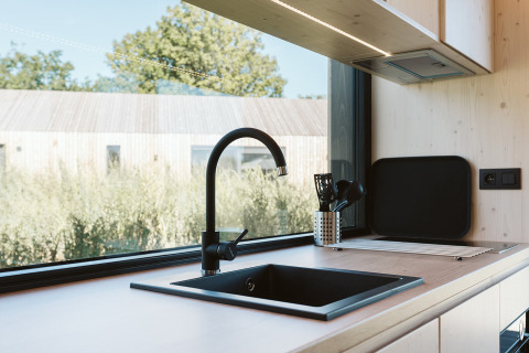 Moderne tiny house keuken met zwart kraan en groot raam, gelegen in De Klepperstee vakantiepark, Nederland.