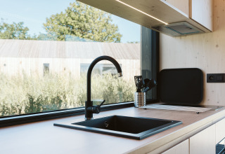 Modern tiny house kitchen sink with black faucet and large window at De Klepperstee holiday park, Netherlands.