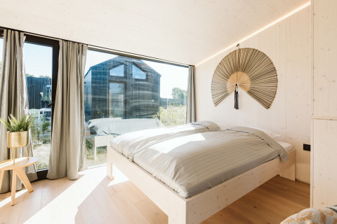 Dormitorio luminoso en la tiny house Backer del Holiday park De Klepperstee en los Países Bajos, con gran ventanal.