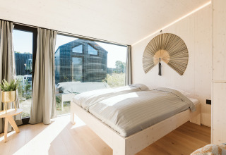 Dormitorio luminoso en la tiny house Backer del Holiday park De Klepperstee en los Países Bajos, con gran ventanal.