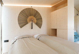 Dormitorio en la tiny house Backer de De Klepperstee con dos camas individuales y gran abanico decorativo en la pared.