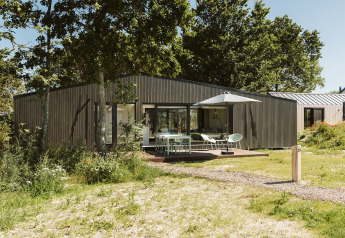 Modern lodge at De Klepperstee holiday park in the Netherlands with wood cladding, patio, and umbrella.